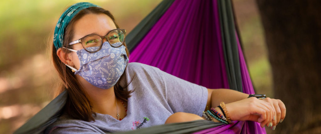 Student hanging out in a hammock wearing a cloth face covering